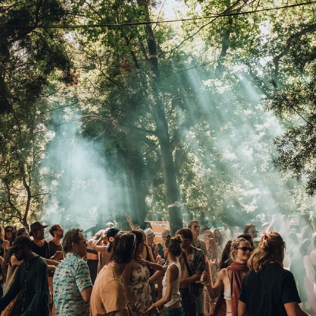 `A photograph of the crowd during the day at Retreat Yourself, with the light shining rays through smoke in the air.